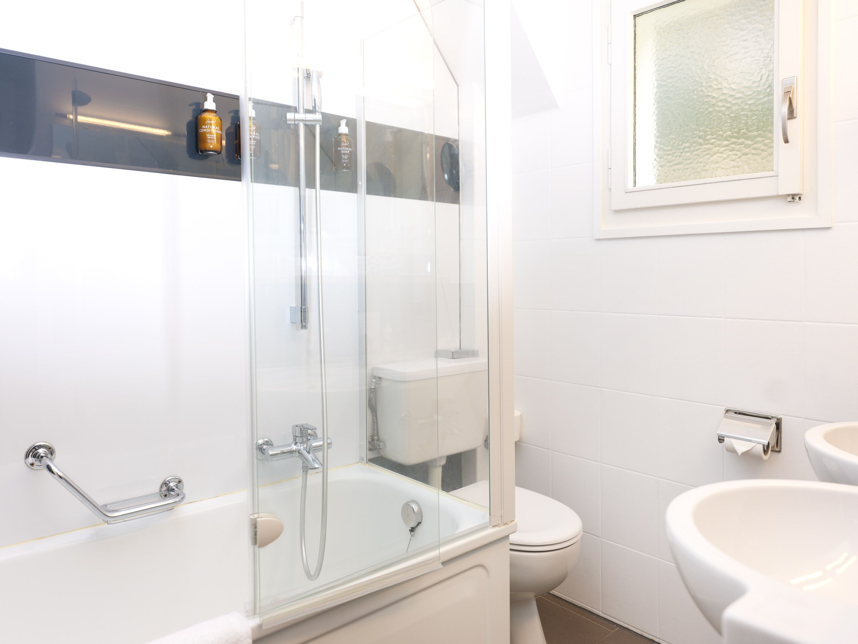 A modern bathroom with a glass-enclosed shower, a white toilet, and a sink.