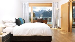 Een moderne slaapkamer met een groot bed, houten vloeren en uitzicht op bergen door een glazen deur.