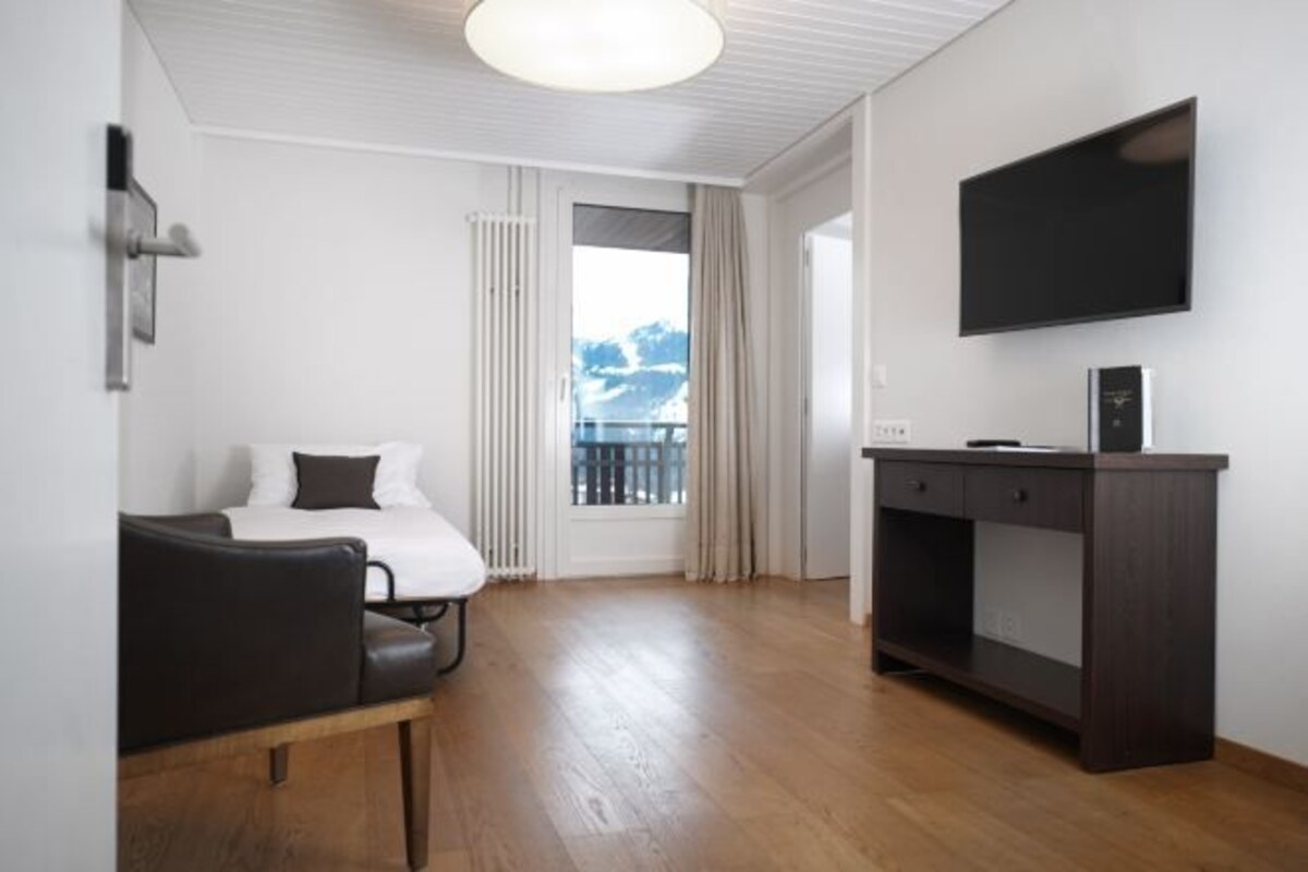 A hotel room with a bed, a desk, a chair, a TV, and a view of the outdoors.