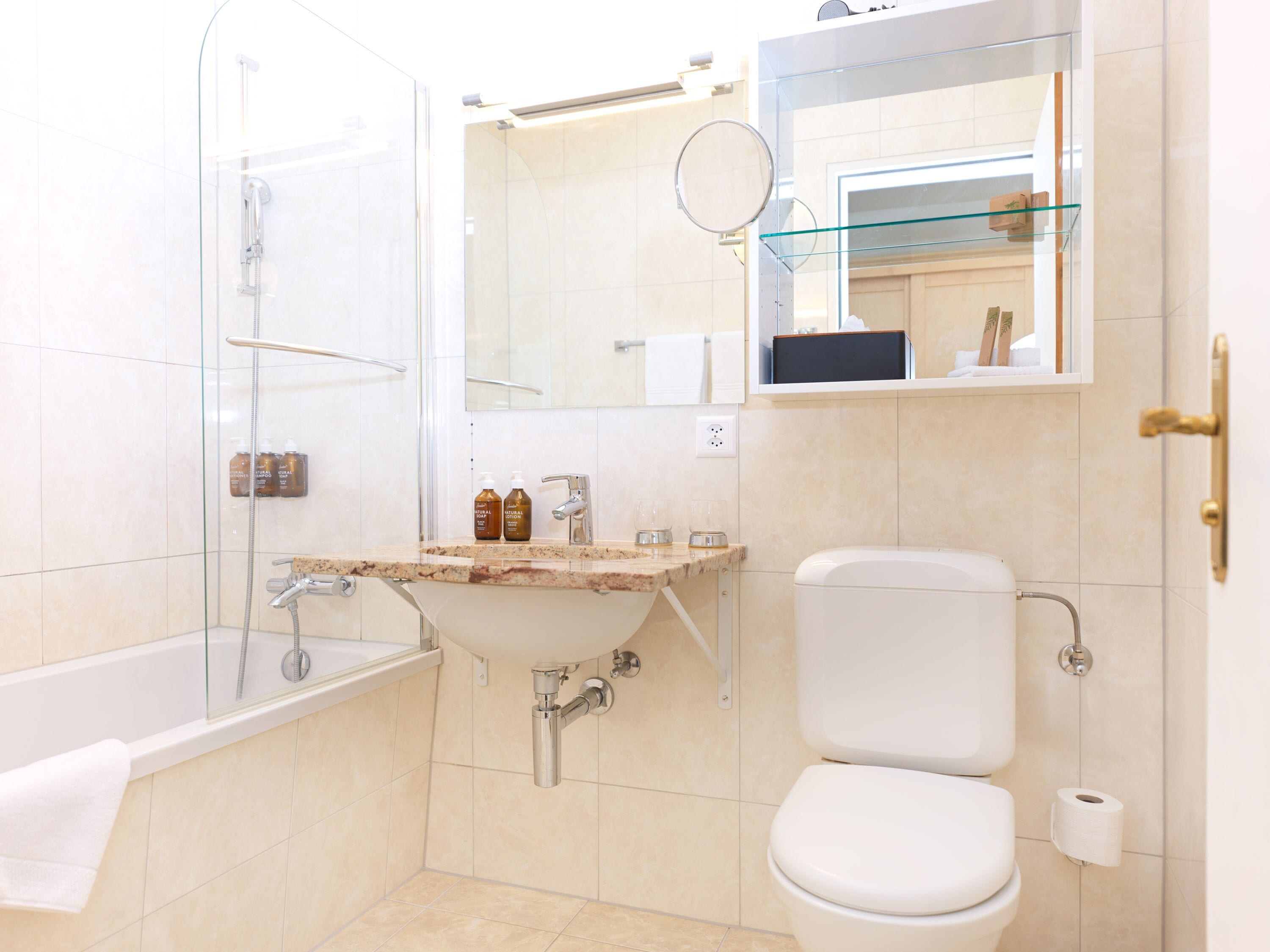 A bathroom with a glass shower enclosure, a sink with toiletries, a toilet, and a mirror.