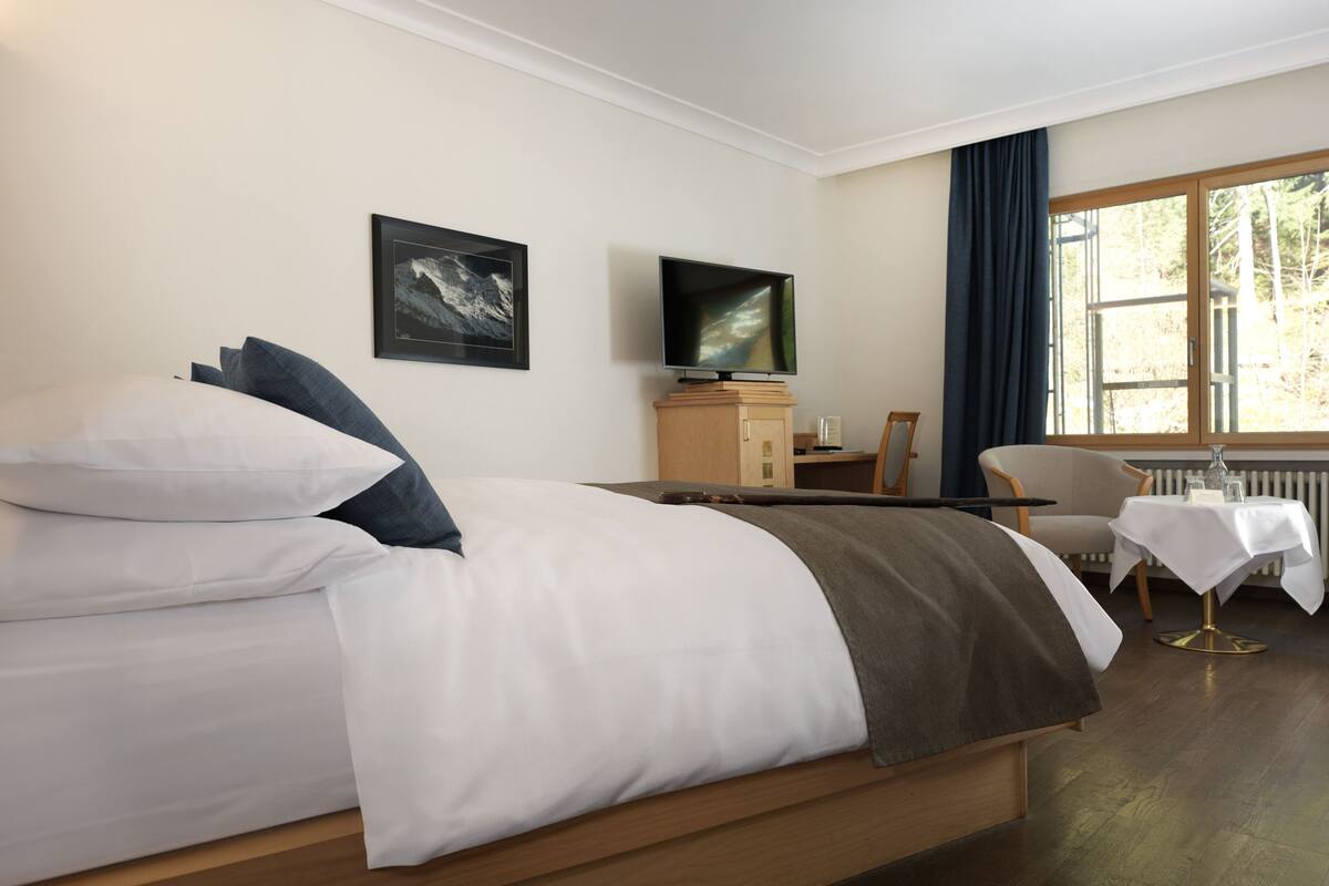 Ein Hotelzimmer mit Bett, Schreibtisch, Stuhl, Fernseher und einem Fenster mit Vorhängen.