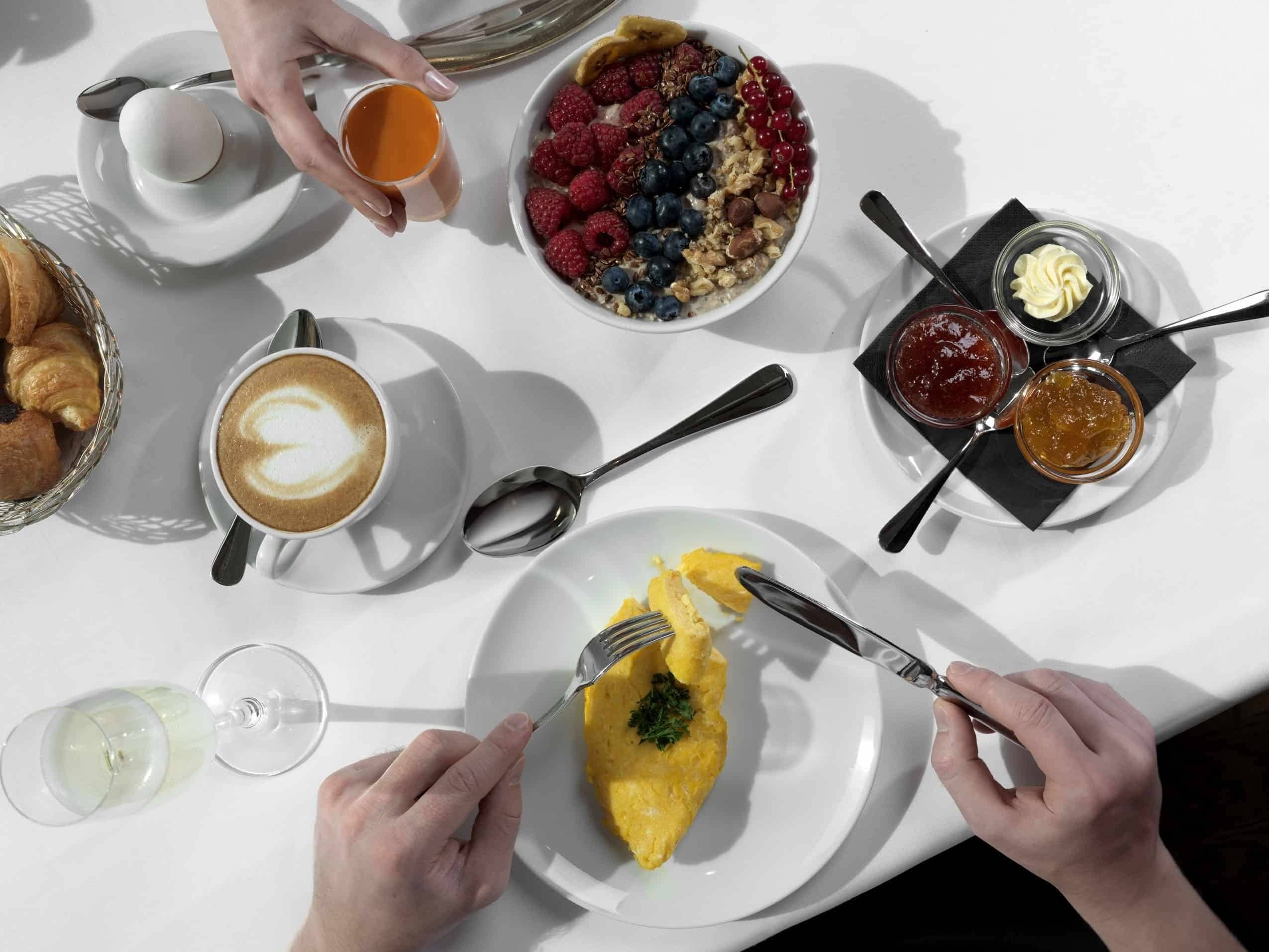 A breakfast setting with croissants, coffee, a bowl of fruit, and a glass of wine on a white table.