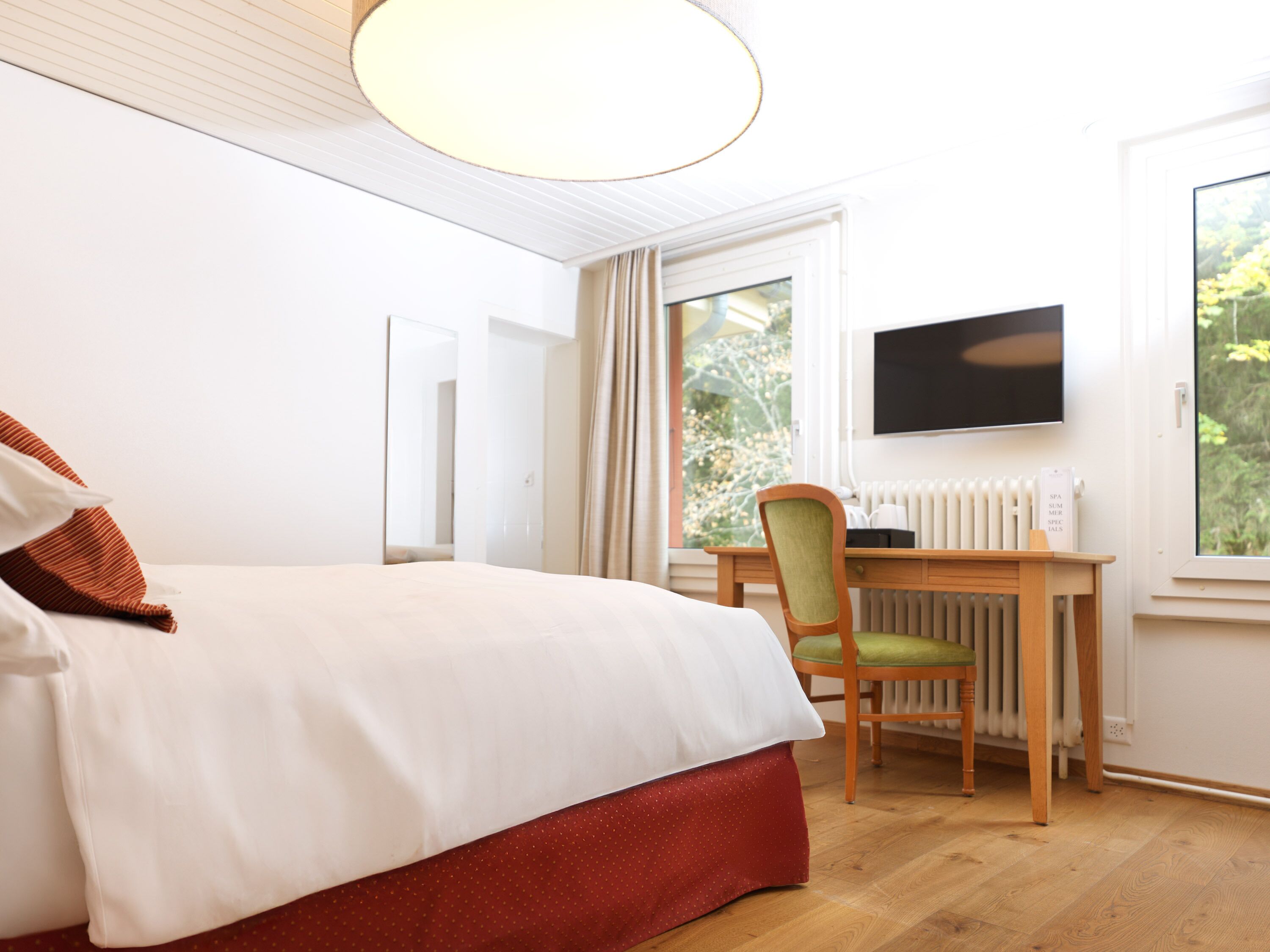 Une chambre d’hôtel équipée d’un lit, d’un bureau, d’une chaise, d’une télévision et d’une fenêtre donnant sur un paysage verdoyant.