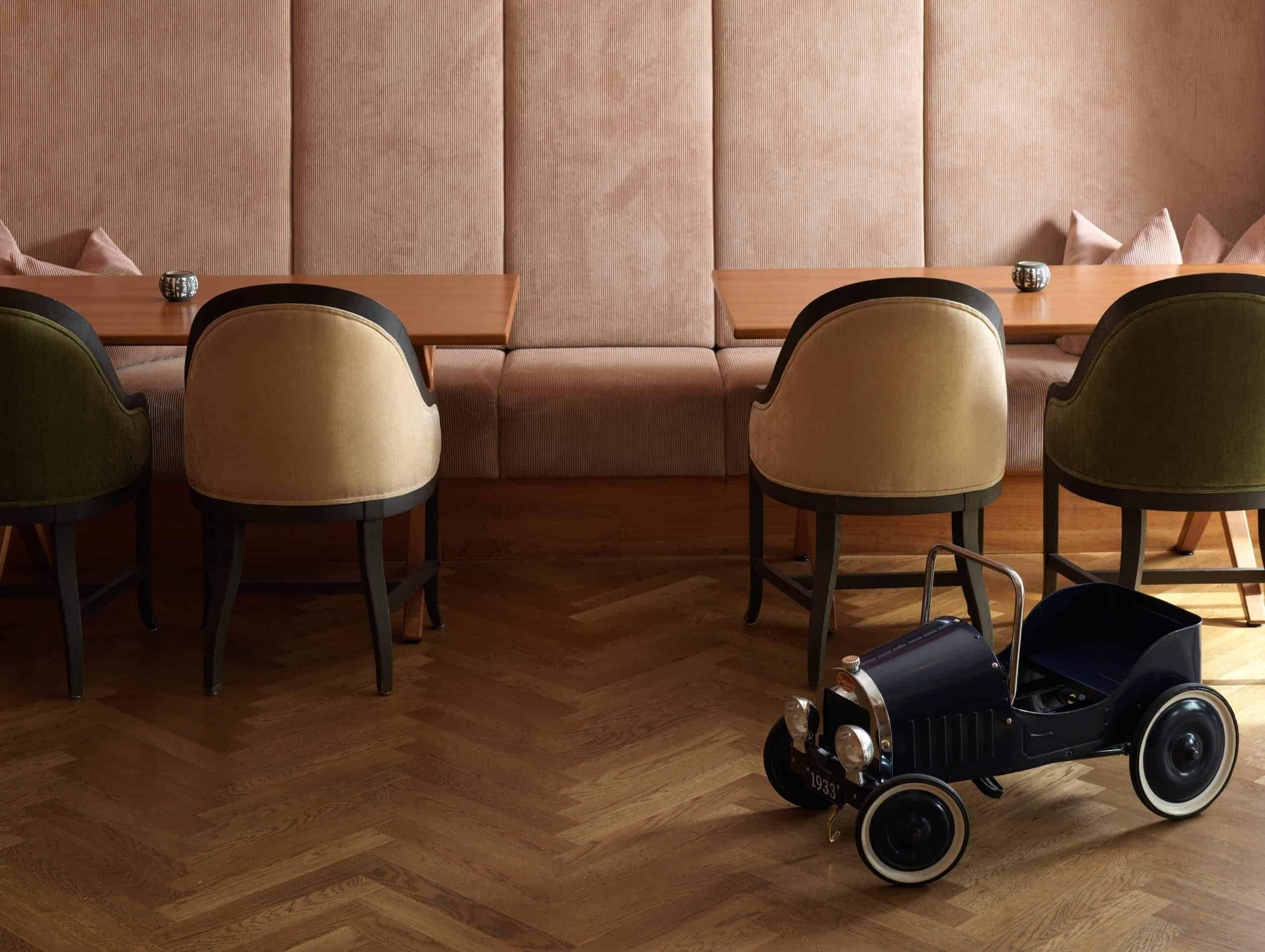 A room with a wooden herringbone floor, a beige sofa, and two chairs with a light brown cushion.