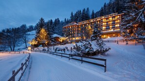 Een meerlaags hotel met balkons, omgeven door met sneeuw bedekte bomen en een houten hek.