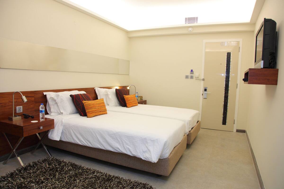 A hotel room with a large bed, bedside tables, a mirror, a TV, and a door.