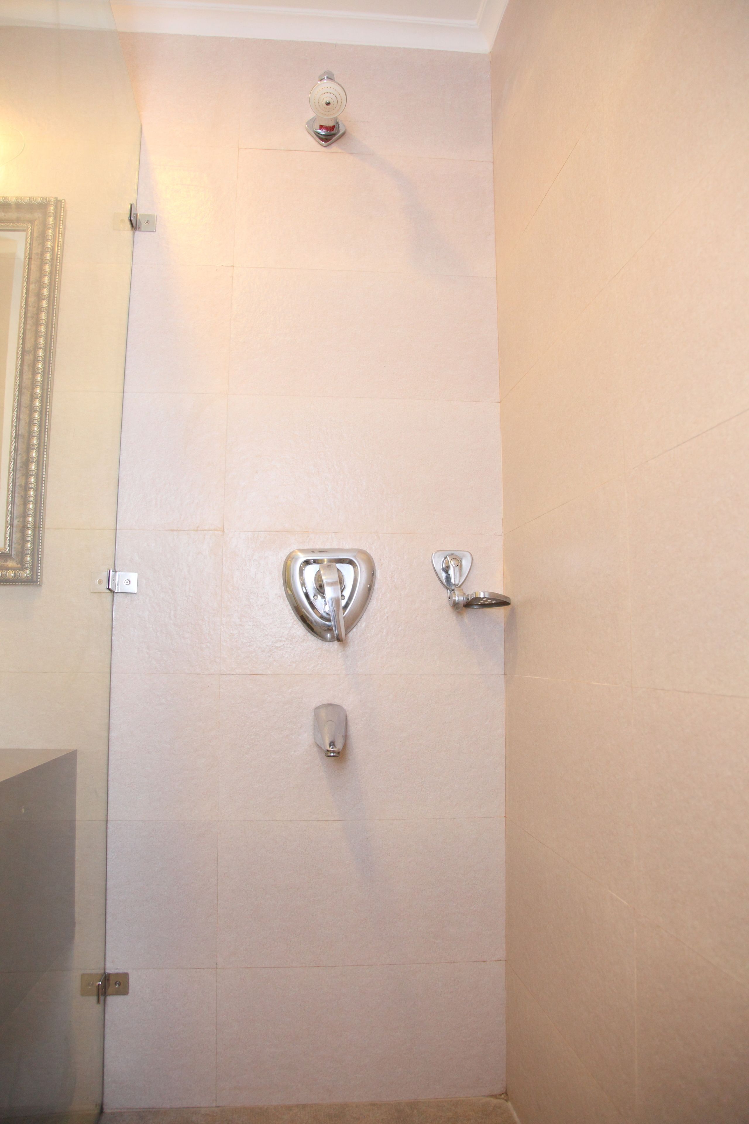 A bathroom with a white tiled wall, a mirror, and a shower door with a chrome handle.