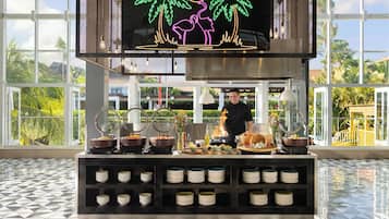 A breakfast buffet setup with various food items and a chef preparing food.