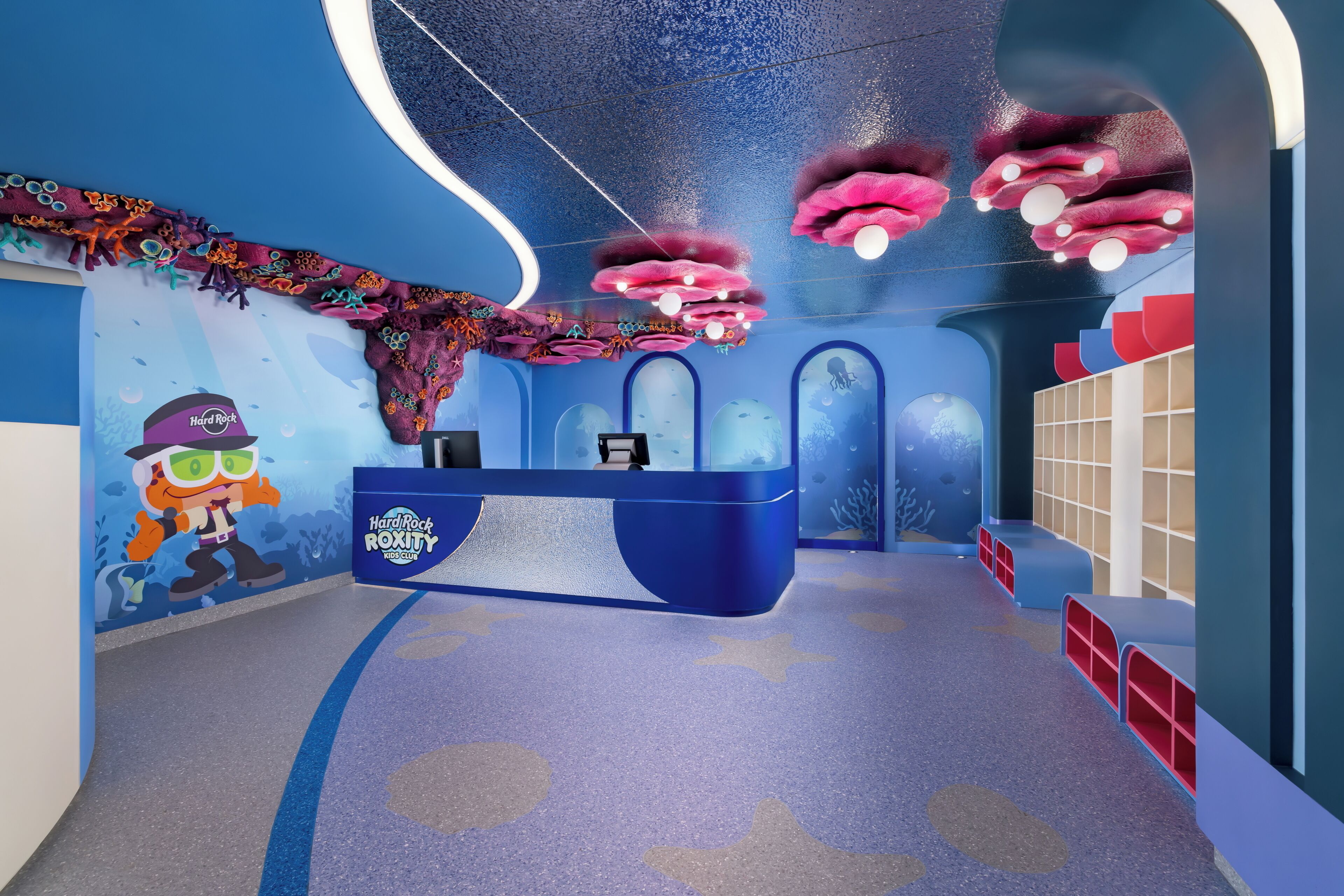 A children's play area with a blue and purple color scheme, featuring a reception desk, aquarium displays, and playful wall decorations.