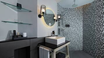 A modern bathroom with a glass shelf, a round mirror, a black countertop, and a shower area with a tiled wall.