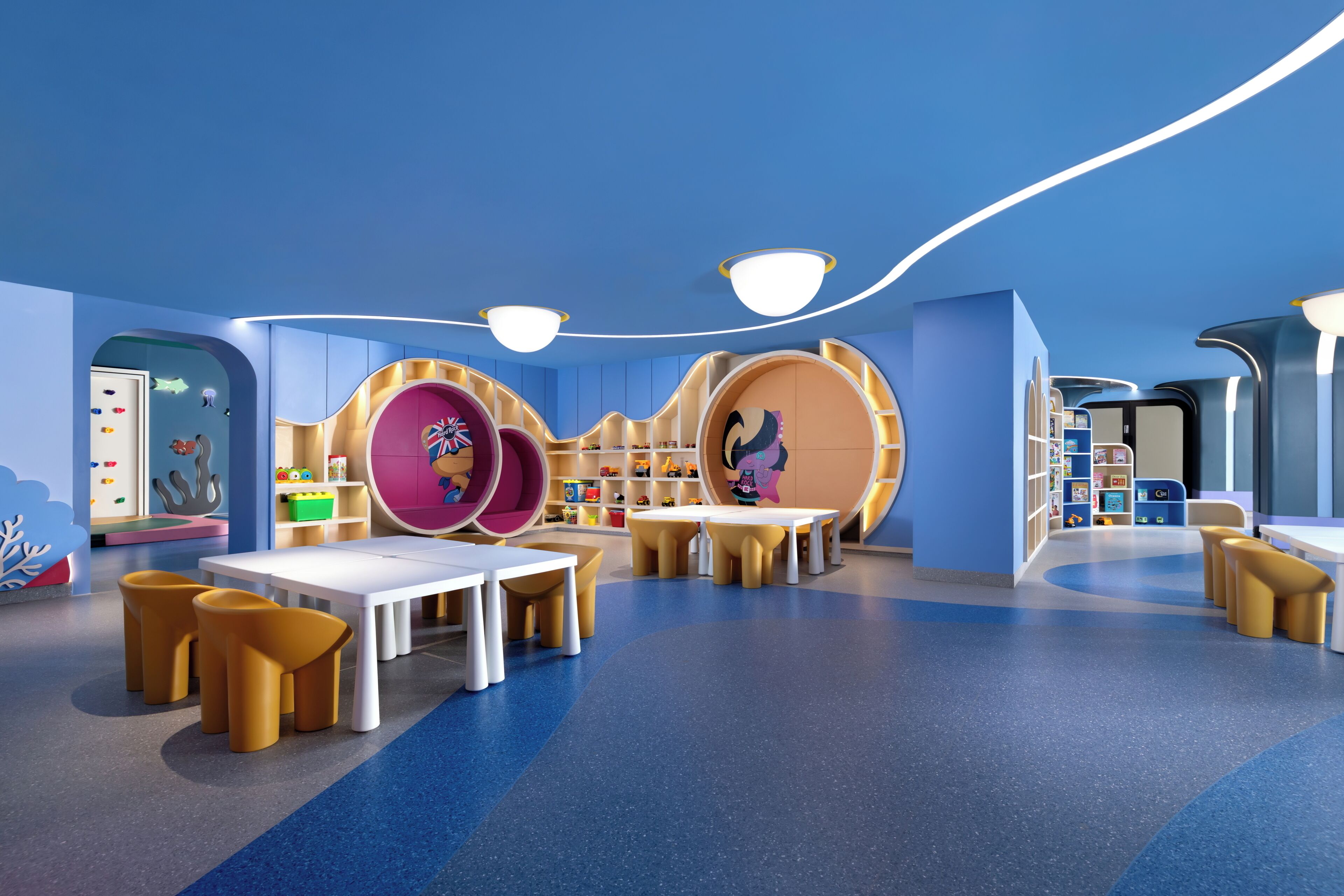 Sala de juegos infantiles con asientos redondos, mesas y estanterías llenas de juguetes.