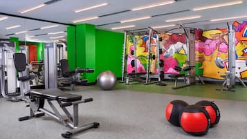 A gym with various exercise equipment, a green wall, and a colorful mural.