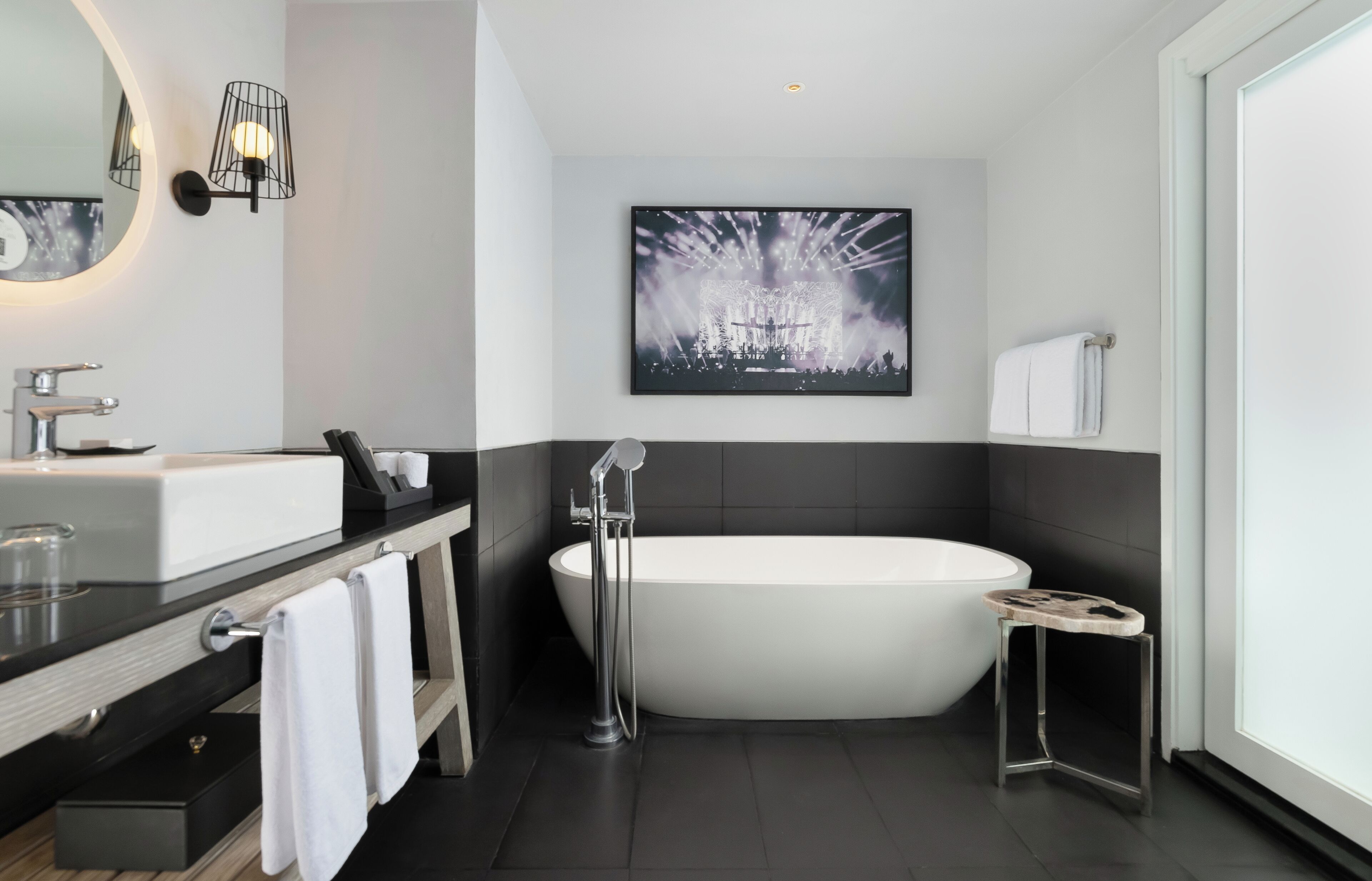 A modern bathroom with a freestanding bathtub, a large mirror, and a framed artwork on the wall.