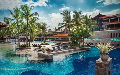 A resort pool area with palm trees, lounge chairs, and a clear blue pool.