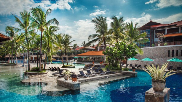 Ein Poolbereich eines Resorts mit Palmen, Liegestühlen und einem klaren, blauen Pool.