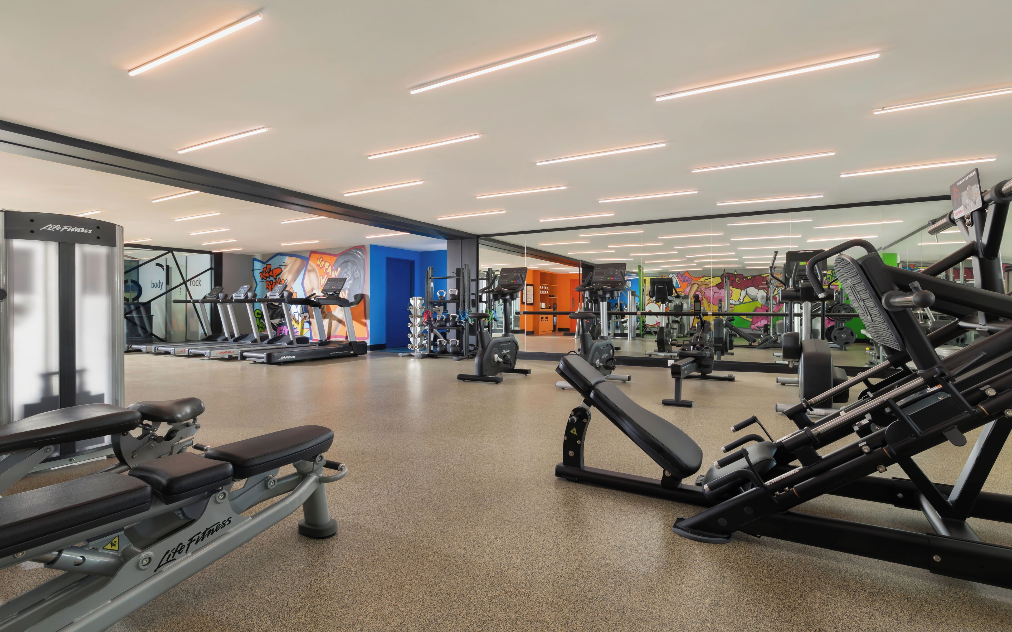 A gym with treadmills, weight machines, and a mirror wall.