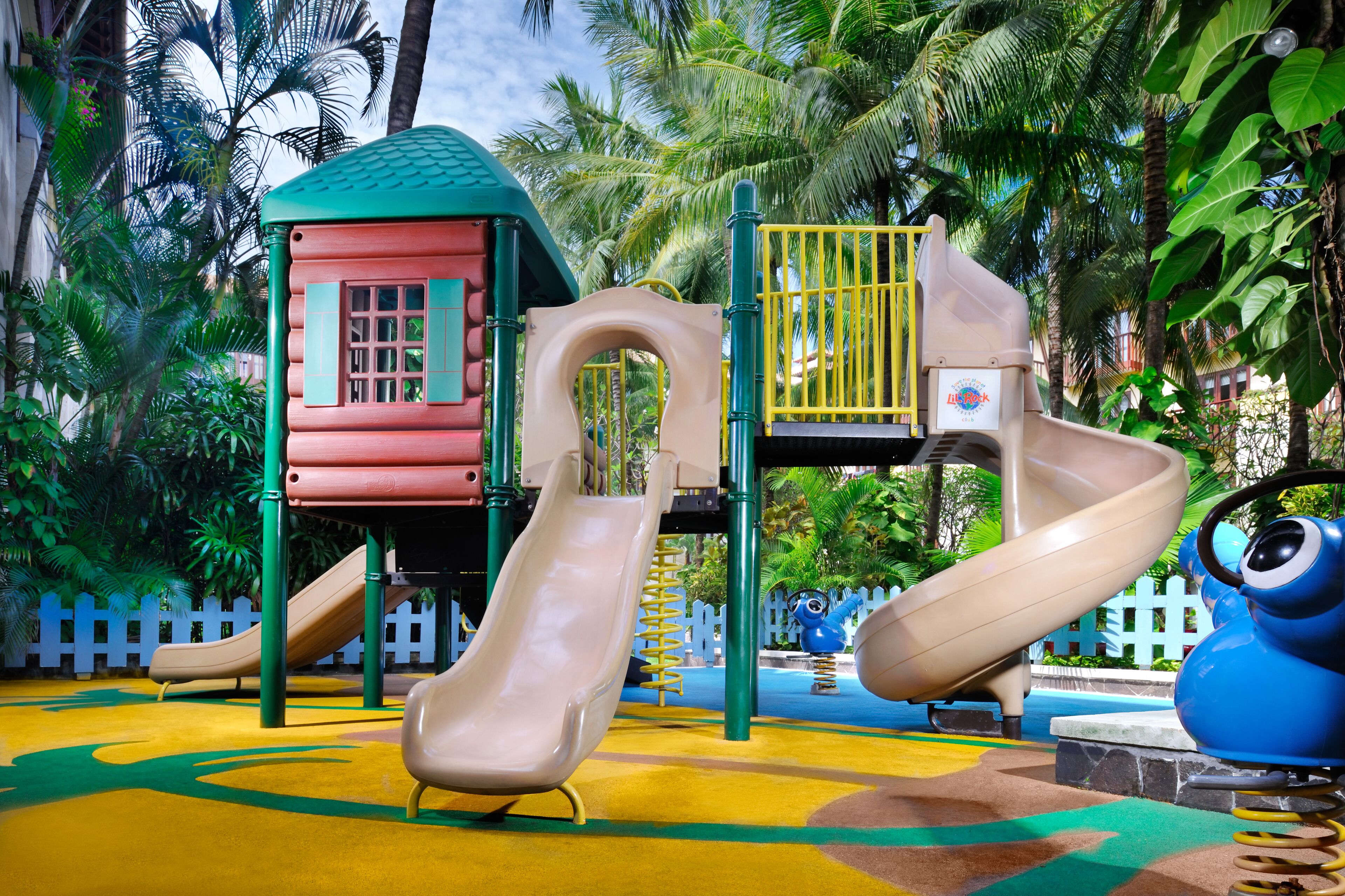 A playground with slides and a climbing structure surrounded by palm trees.