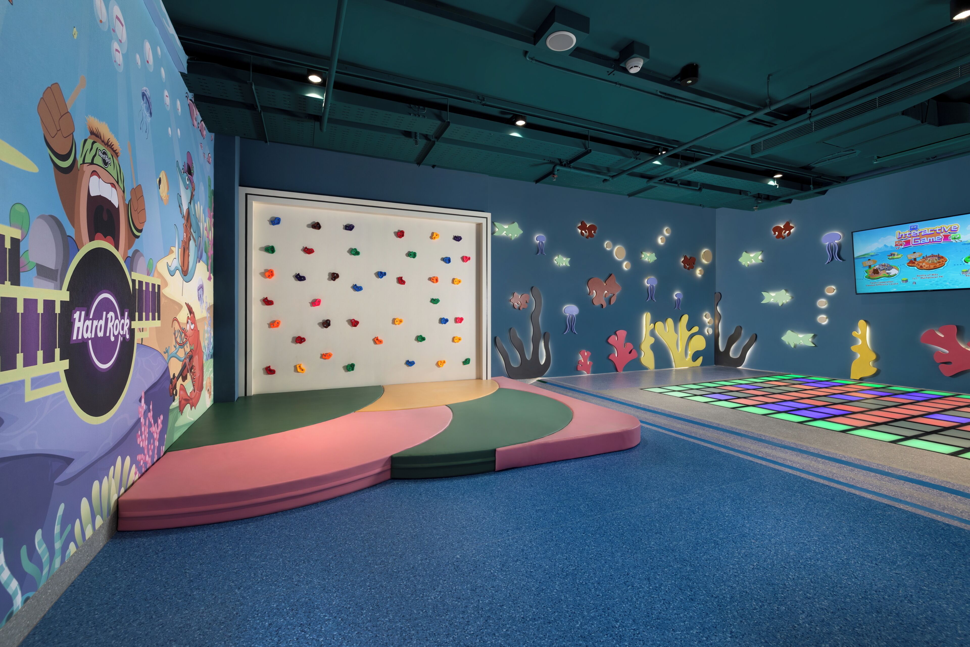 An indoor play area with colorful climbing walls, a stage, and a projected game screen.