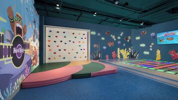 An indoor play area with colorful climbing walls, a stage, and a projected game screen.