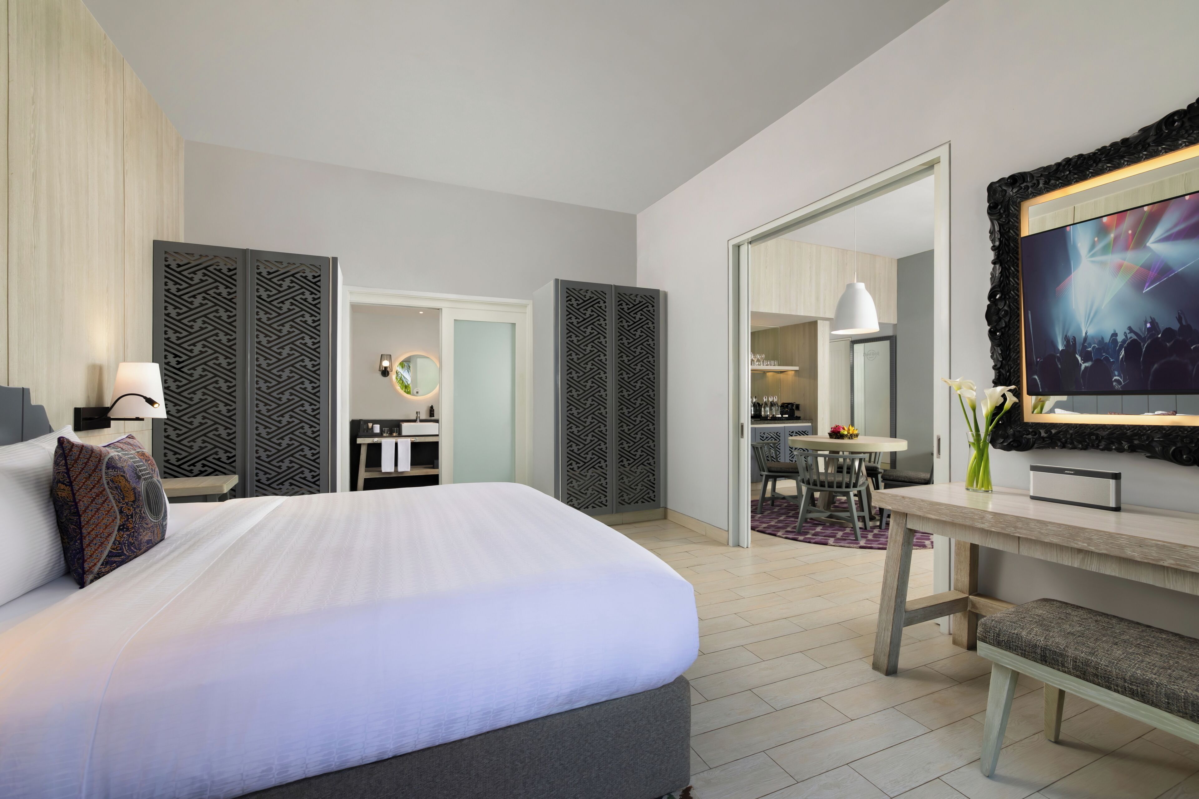 A modern hotel room with a large bed, a desk, a dining area, and a bathroom.