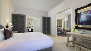 A modern hotel room with a large bed, a desk, a dining area, and a bathroom.