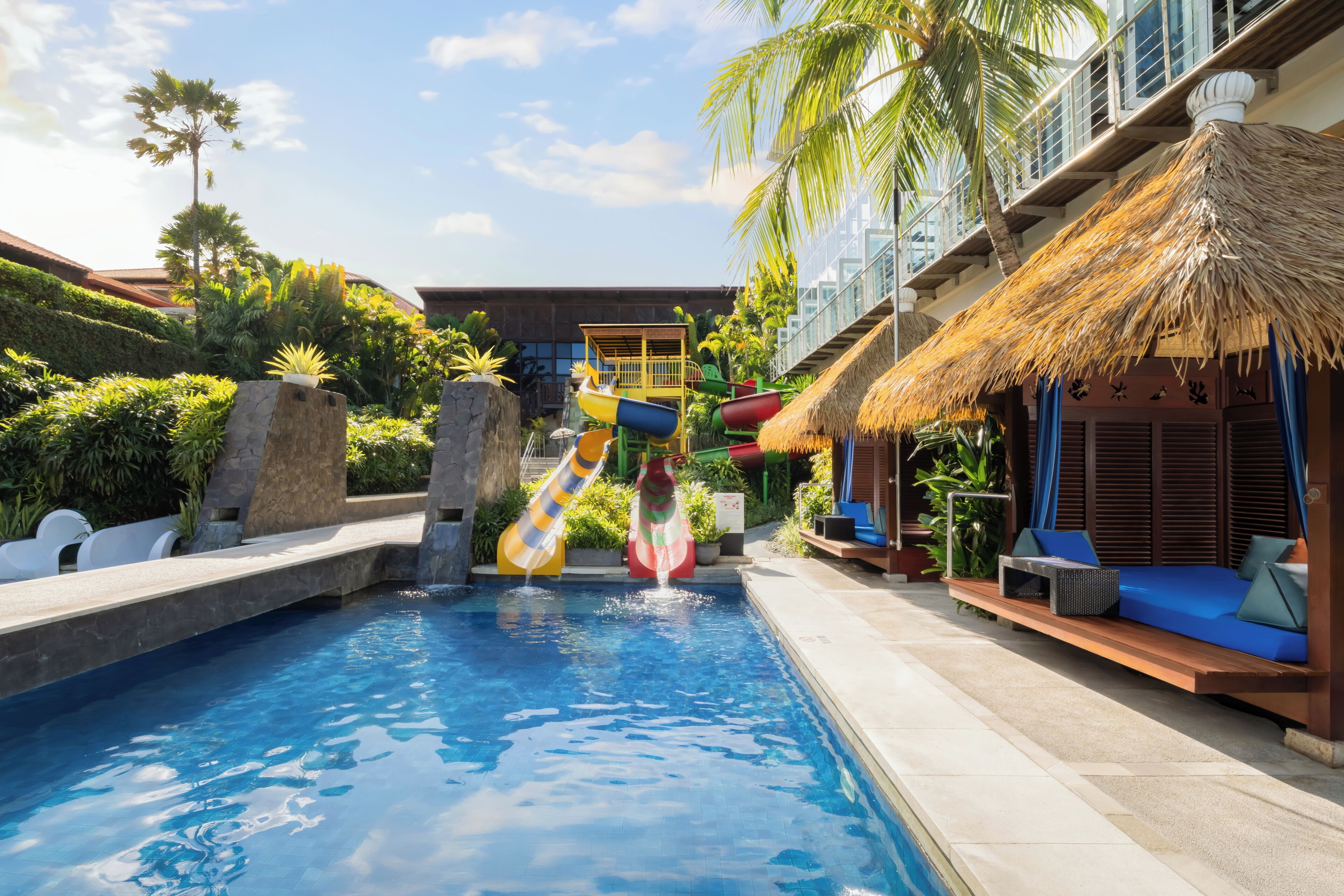 A swimming pool with slides, a thatched-roof structure, and a seating area with cushions.
