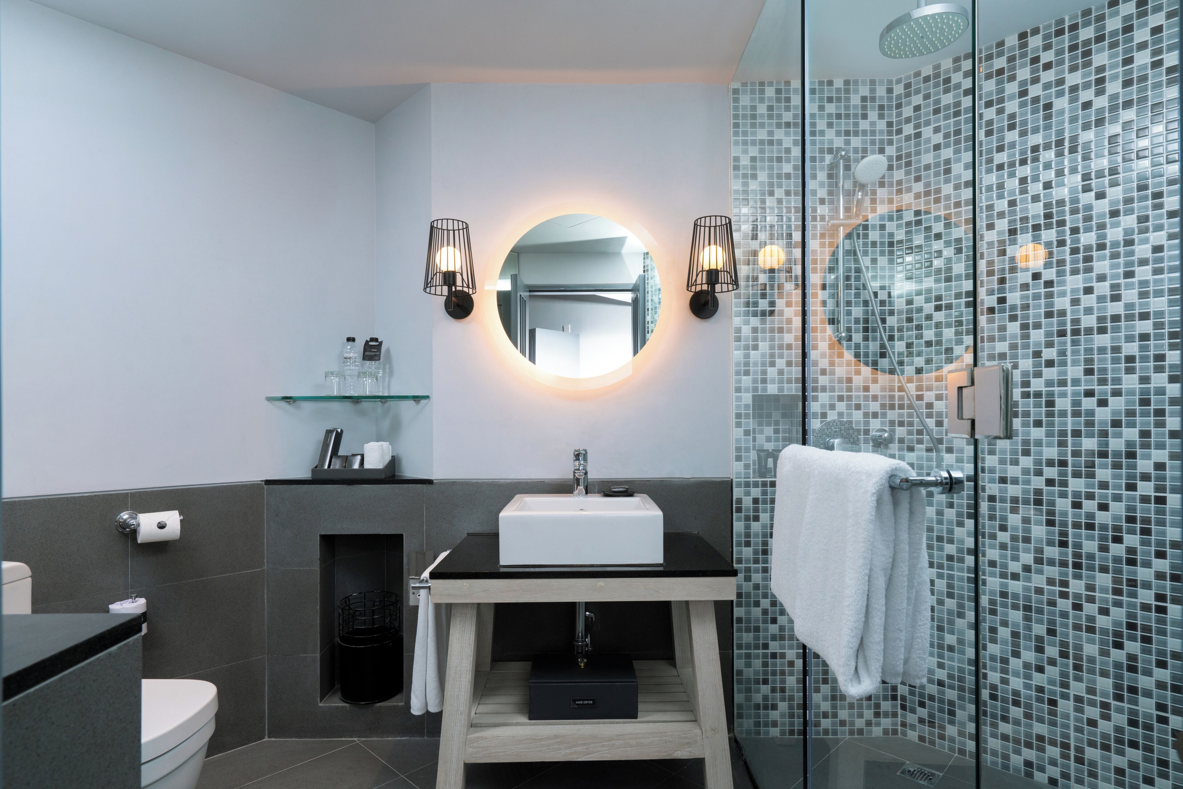 A modern bathroom with a glass shower enclosure, a round mirror, and a white sink.