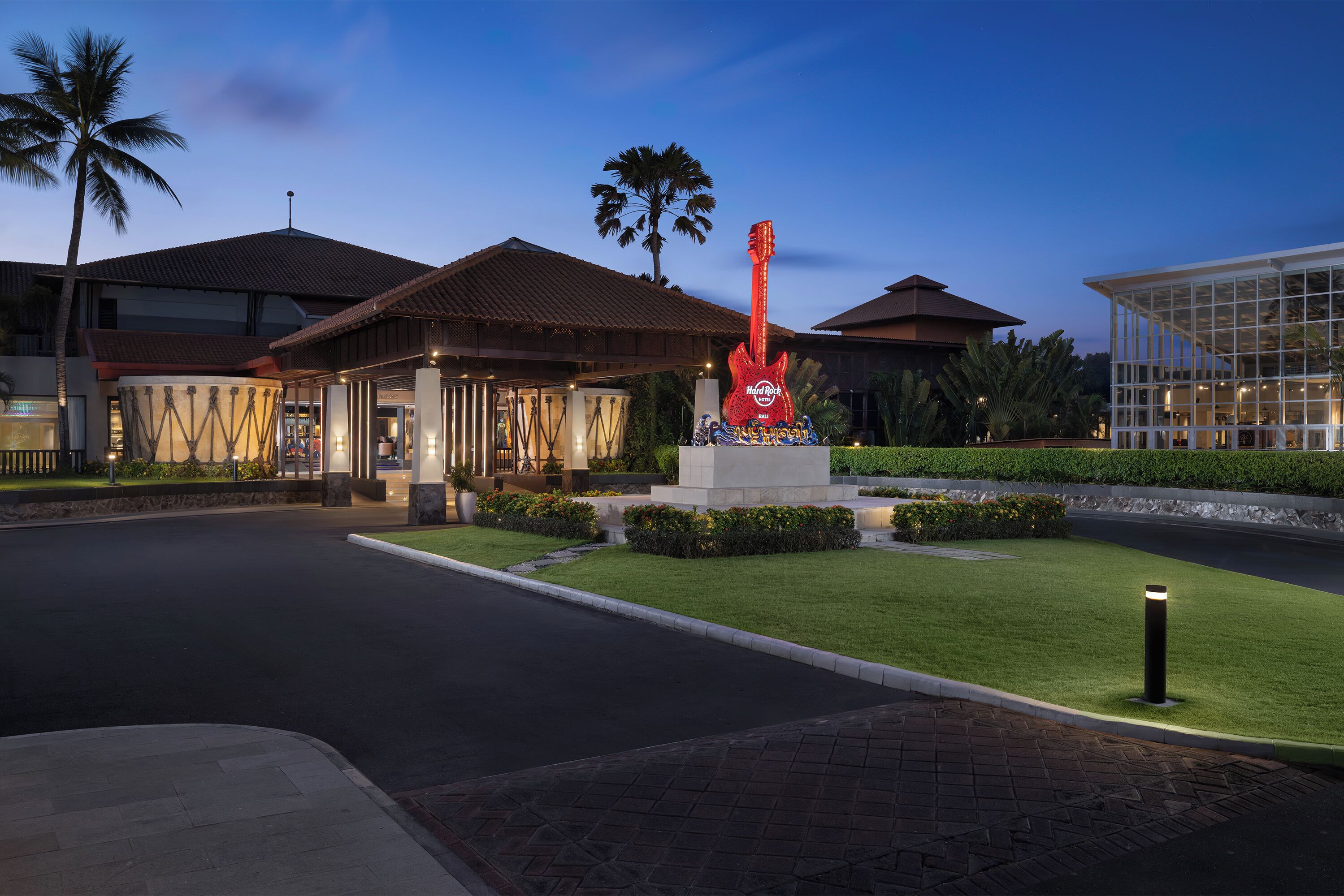 A hotel entrance with a palm tree, a red guitar sculpture, and a well-maintained lawn.