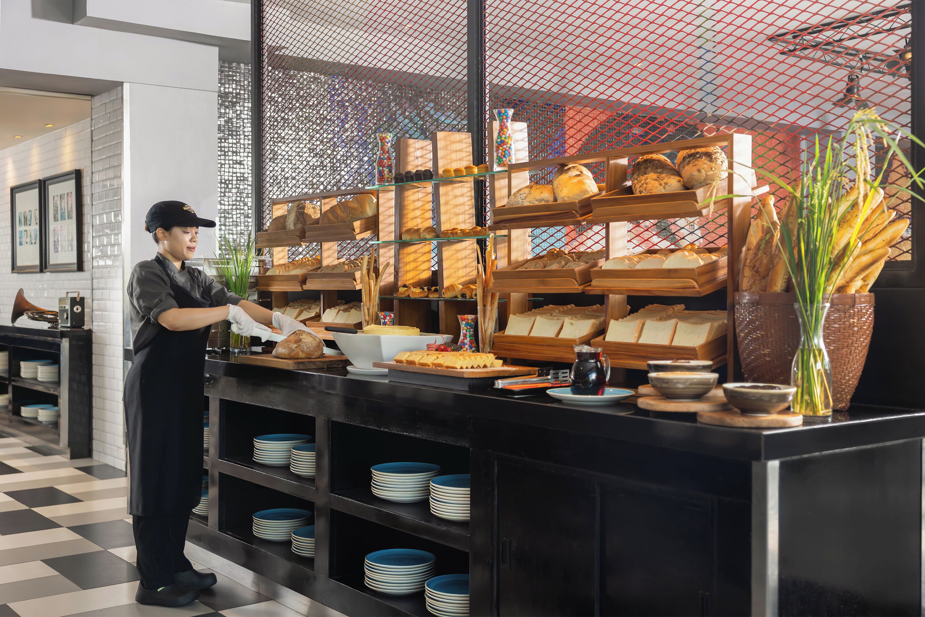 A bakery counter with various breads and pastries, a person serving, and a checkered floor.