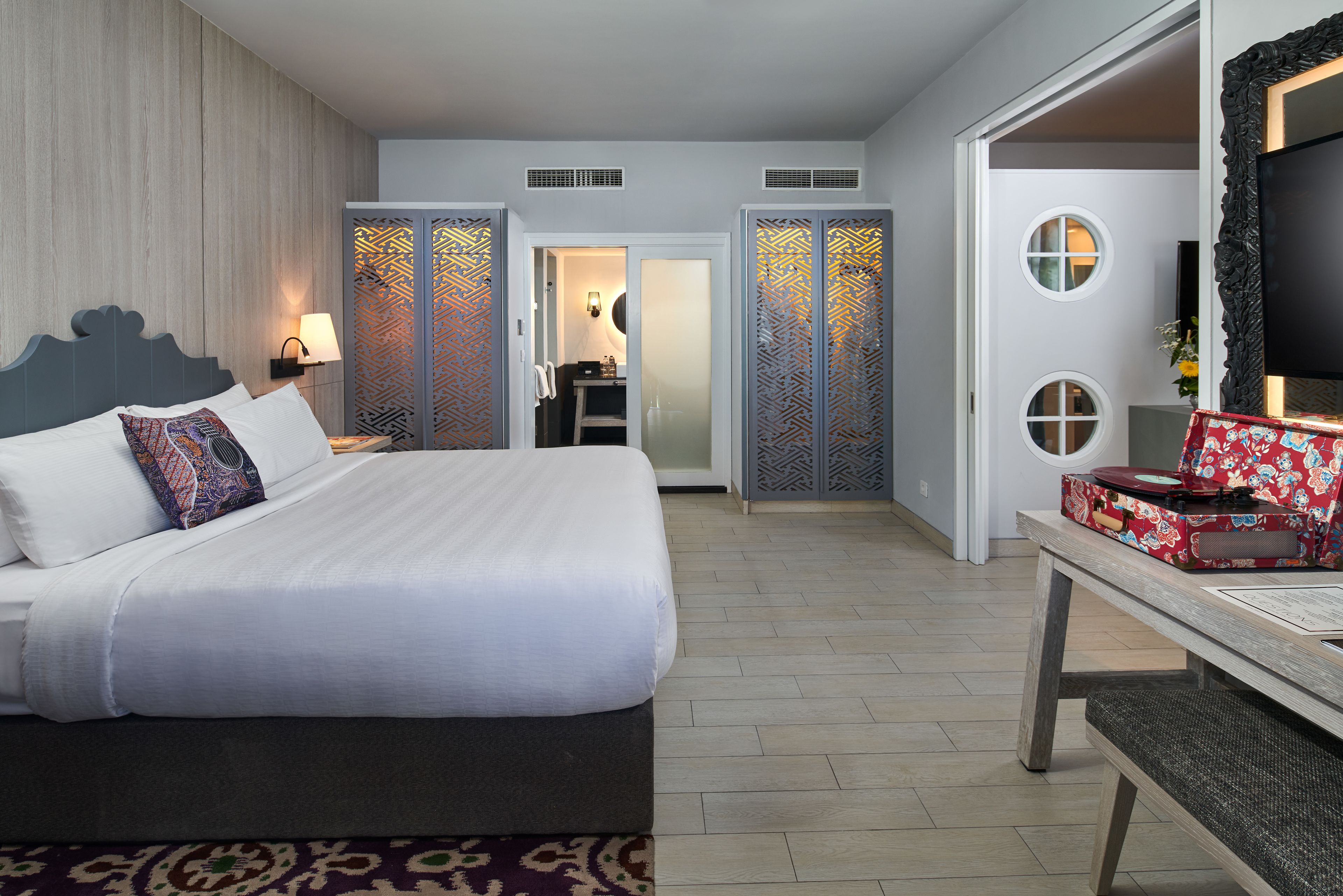 A hotel room with a large bed, a desk with a suitcase, and a TV on a stand.