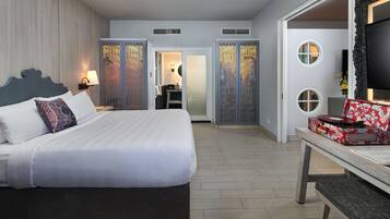 A hotel room with a large bed, a desk with a suitcase, and a TV on a stand.