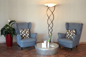Two armchairs with checkered pillows, a round coffee table, a tall floor lamp, and a potted plant.