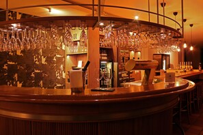 Una zona de bar con una barra curva, varios vasos colgando y estantes llenos de botellas.