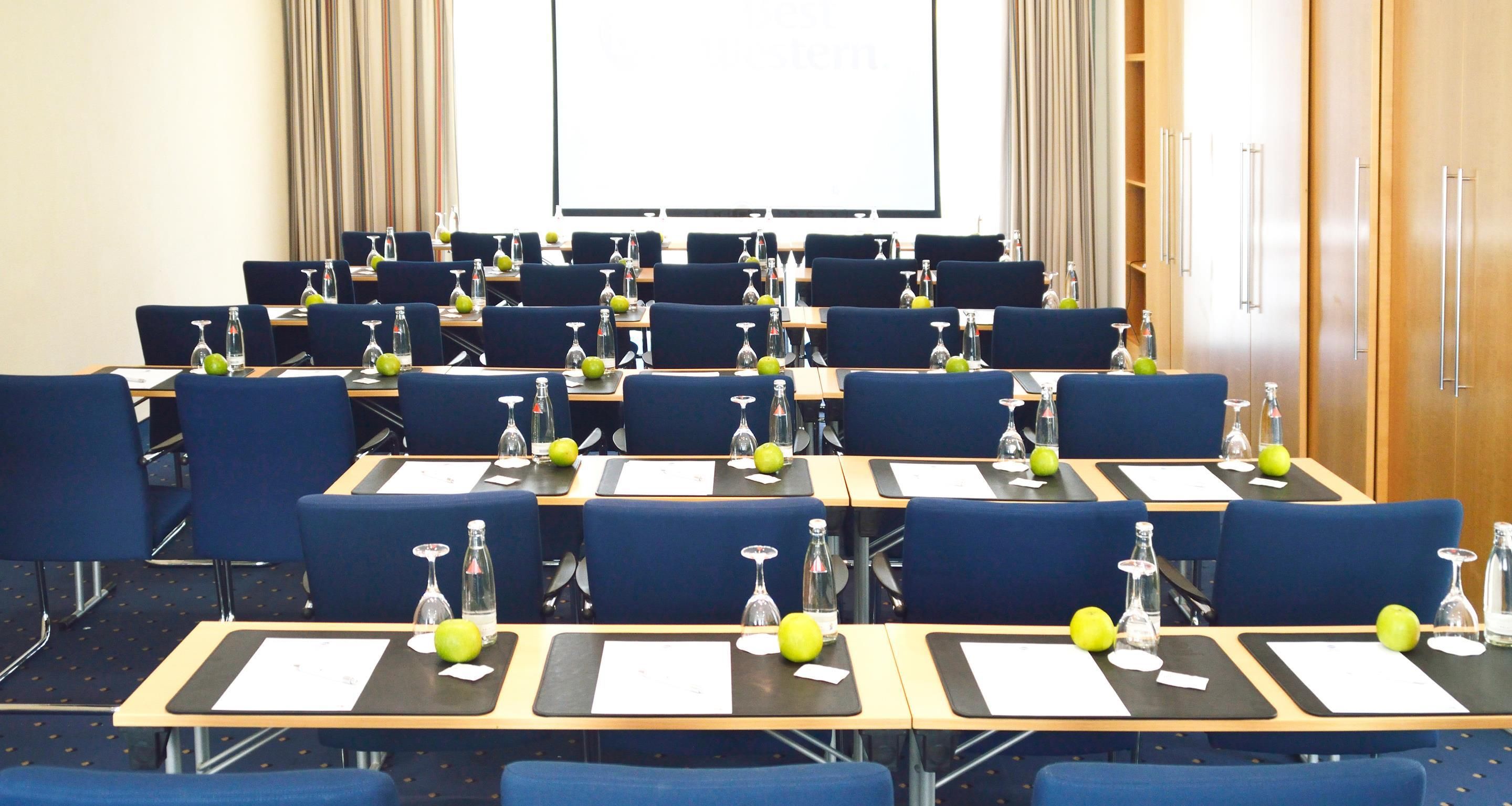 A conference room with rows of tables, chairs, and a projector screen.