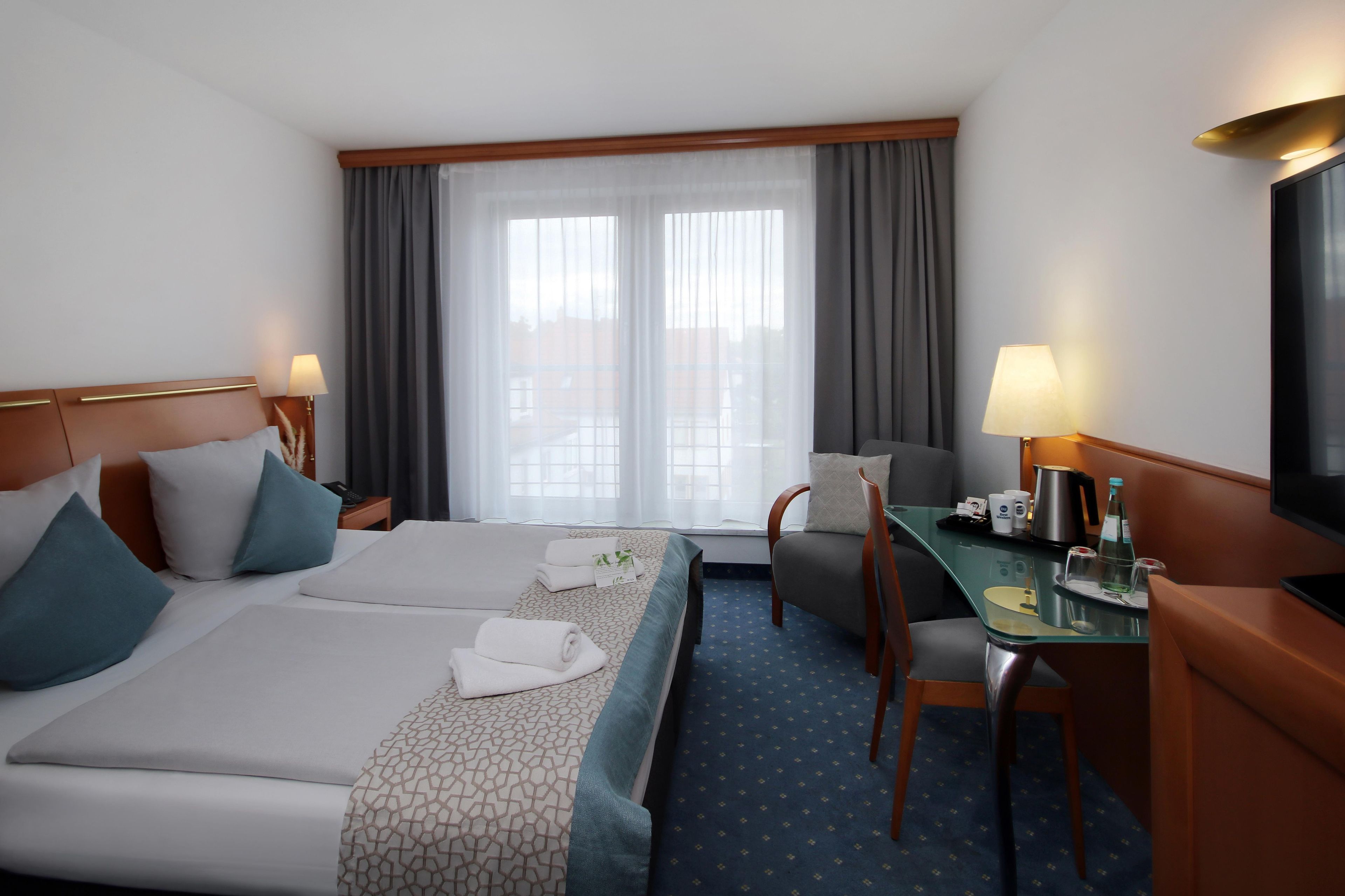 A hotel room with a bed, a desk, a chair, a television, and a window with curtains.