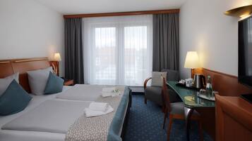 A hotel room with a bed, a desk, a chair, a television, and a window with curtains.