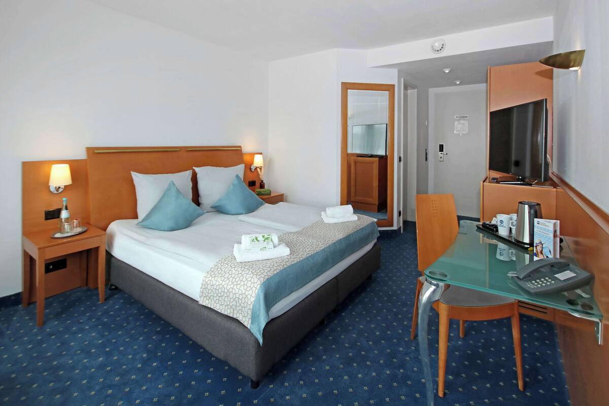 Una habitación de hotel con una cama, mesitas de noche, un escritorio y un teléfono, y un espejo.