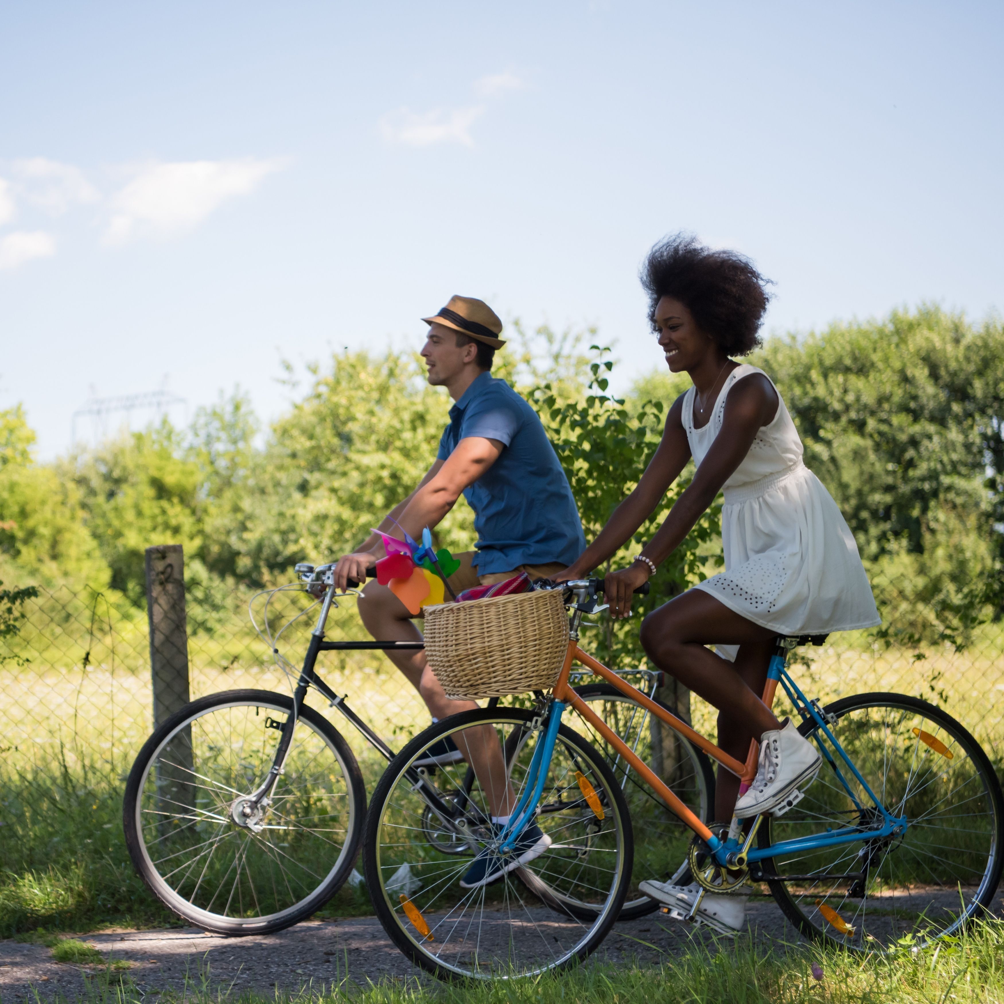 Deux personnes font du vélo sur un chemin bordé de verdure, avec une clôture en arrière-plan.