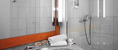 Un baño moderno con cabina de ducha de vidrio, un espejo grande y encimera de granito con artículos de aseo.