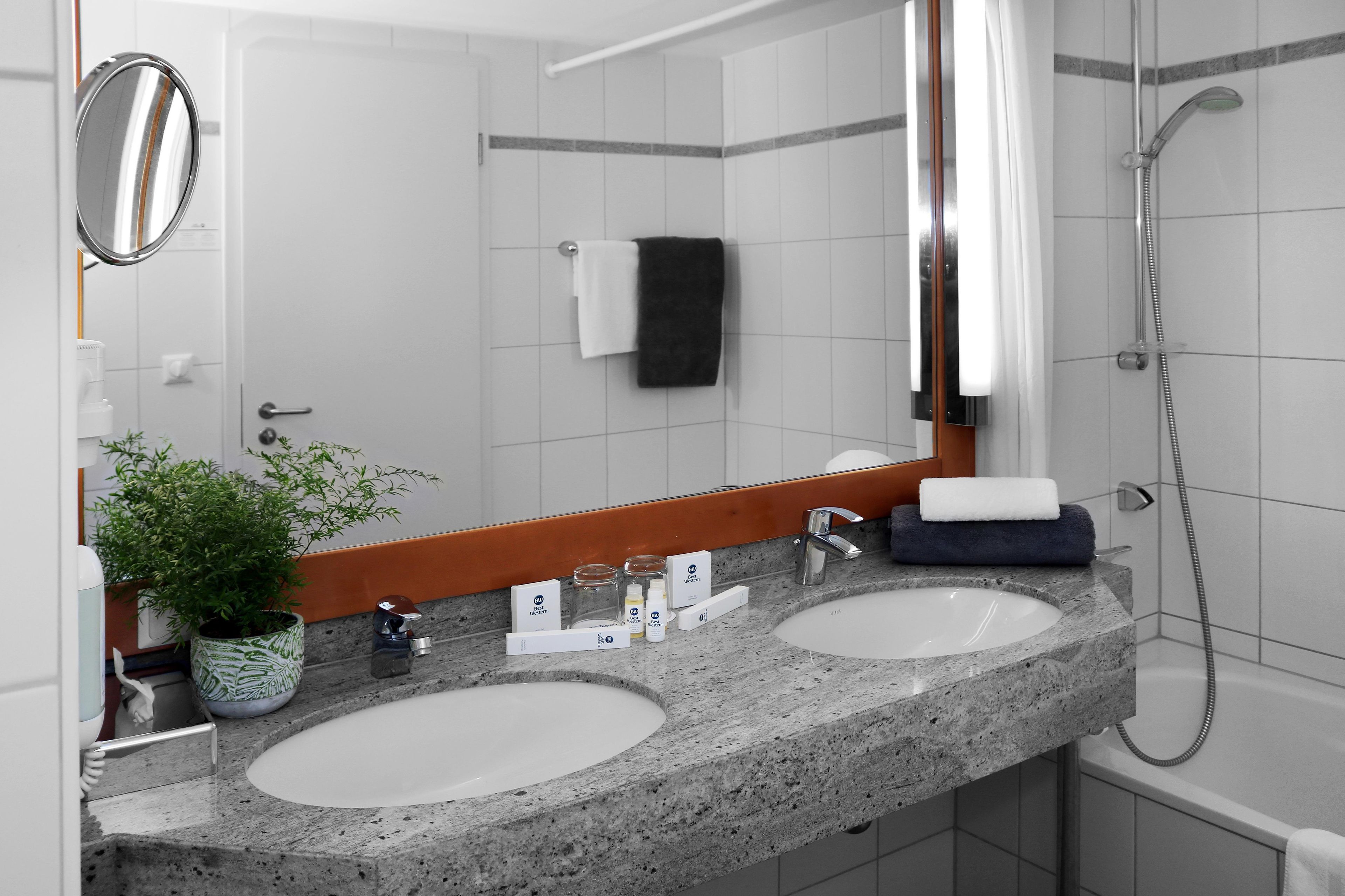 Un baño con dos lavamanos, un espejo, una ducha y una planta en maceta.