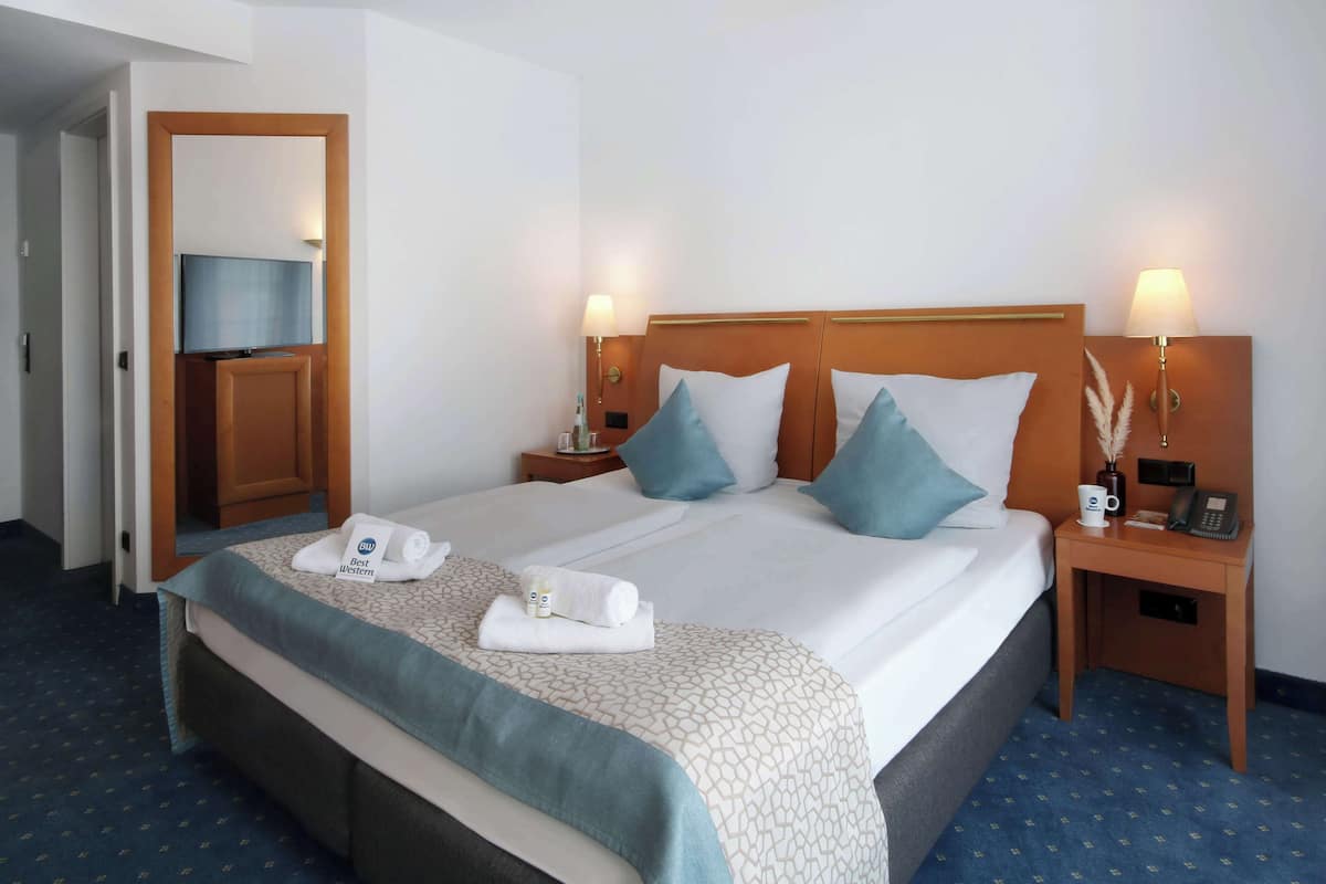Una habitación de hotel con cama, dos mesitas de noche, televisor y puerta que da a otra habitación.