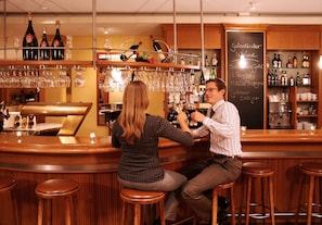 A bar area with wooden stools, a bar counter, and shelves with bottles and glasses.