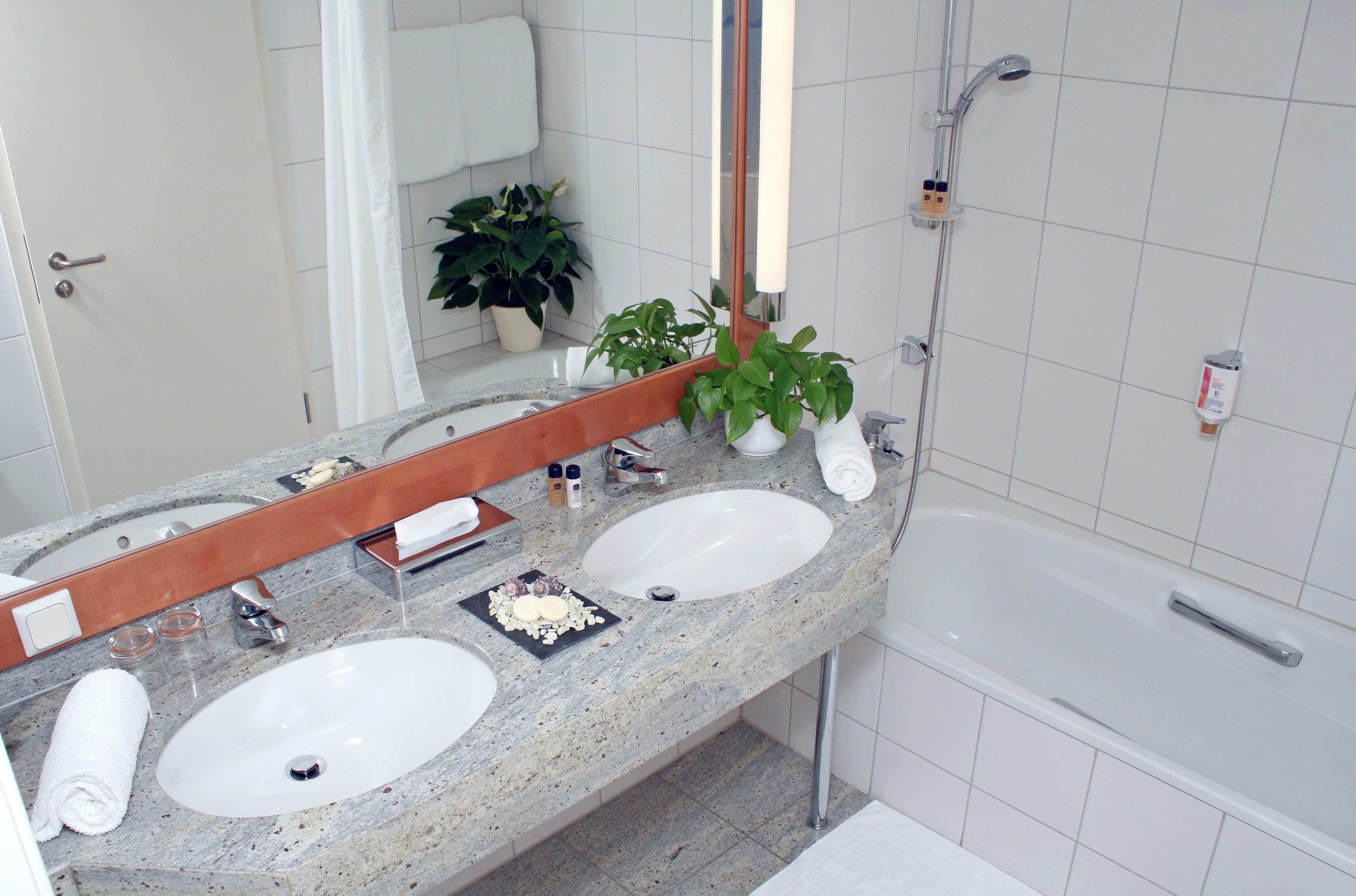 Une salle de bain avec deux lavabos, un miroir, une douche et une plante en pot.