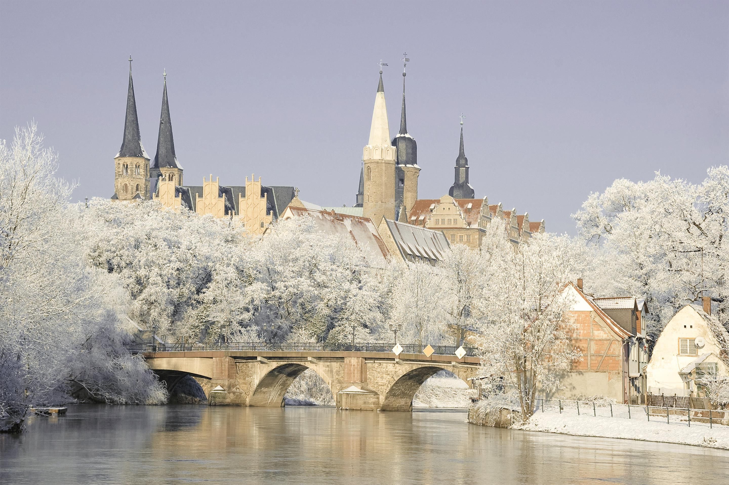 A historic building with multiple spires, a bridge, and frost-covered trees.