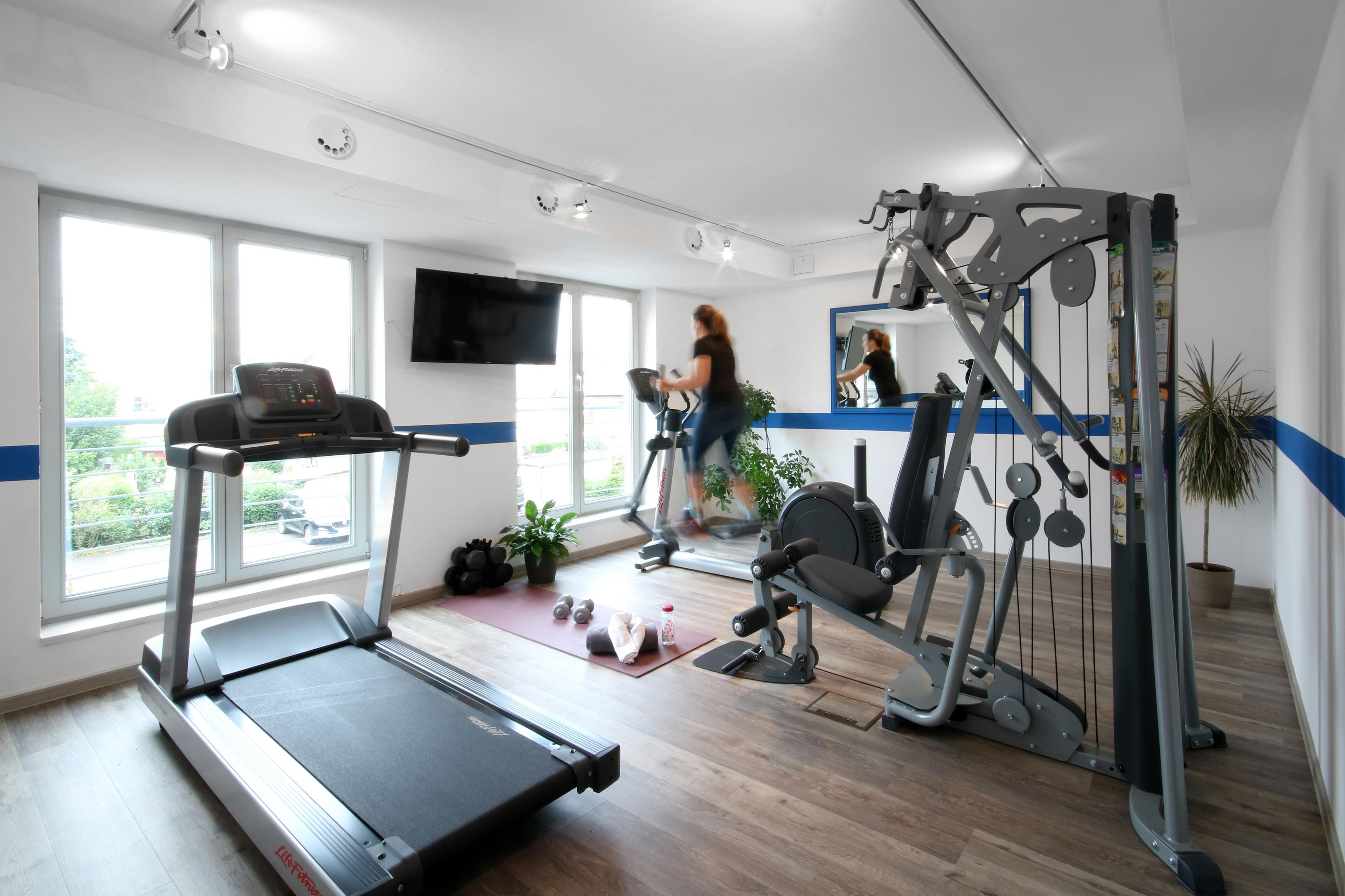 Ein Fitnessstudio mit Laufband, Kraftgeräten und einem Fernseher an der Wand.