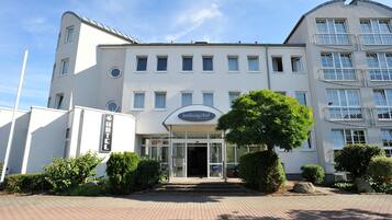 A modern hotel with a white facade, multiple windows, and a prominent entrance.