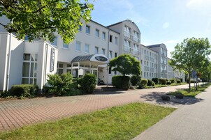 Um hotel moderno com entrada coberta, calçada pavimentada e áreas verdes bem cuidadas.
