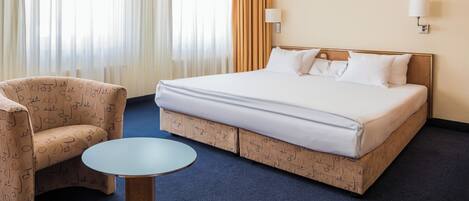 A hotel room with a bed, a chair, a small table, and curtains.
