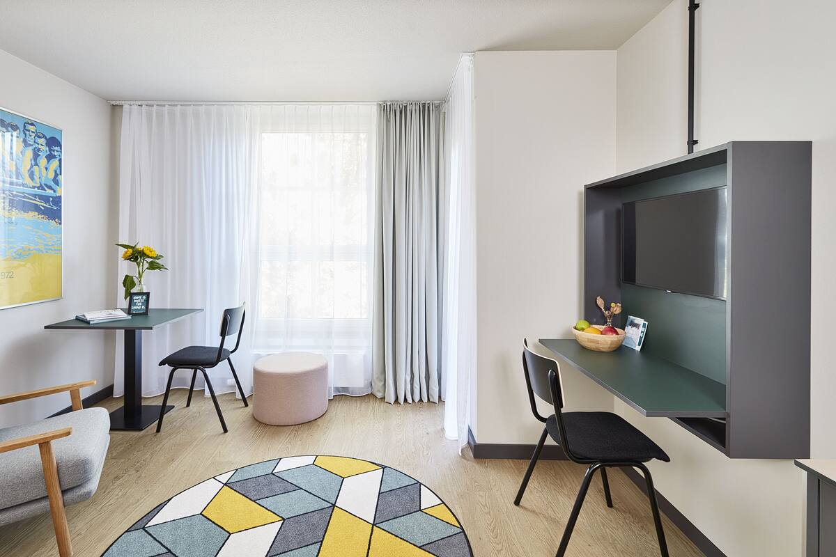A modern, well-lit room with a dining area, a sofa, a coffee table, and a TV mounted on the wall.