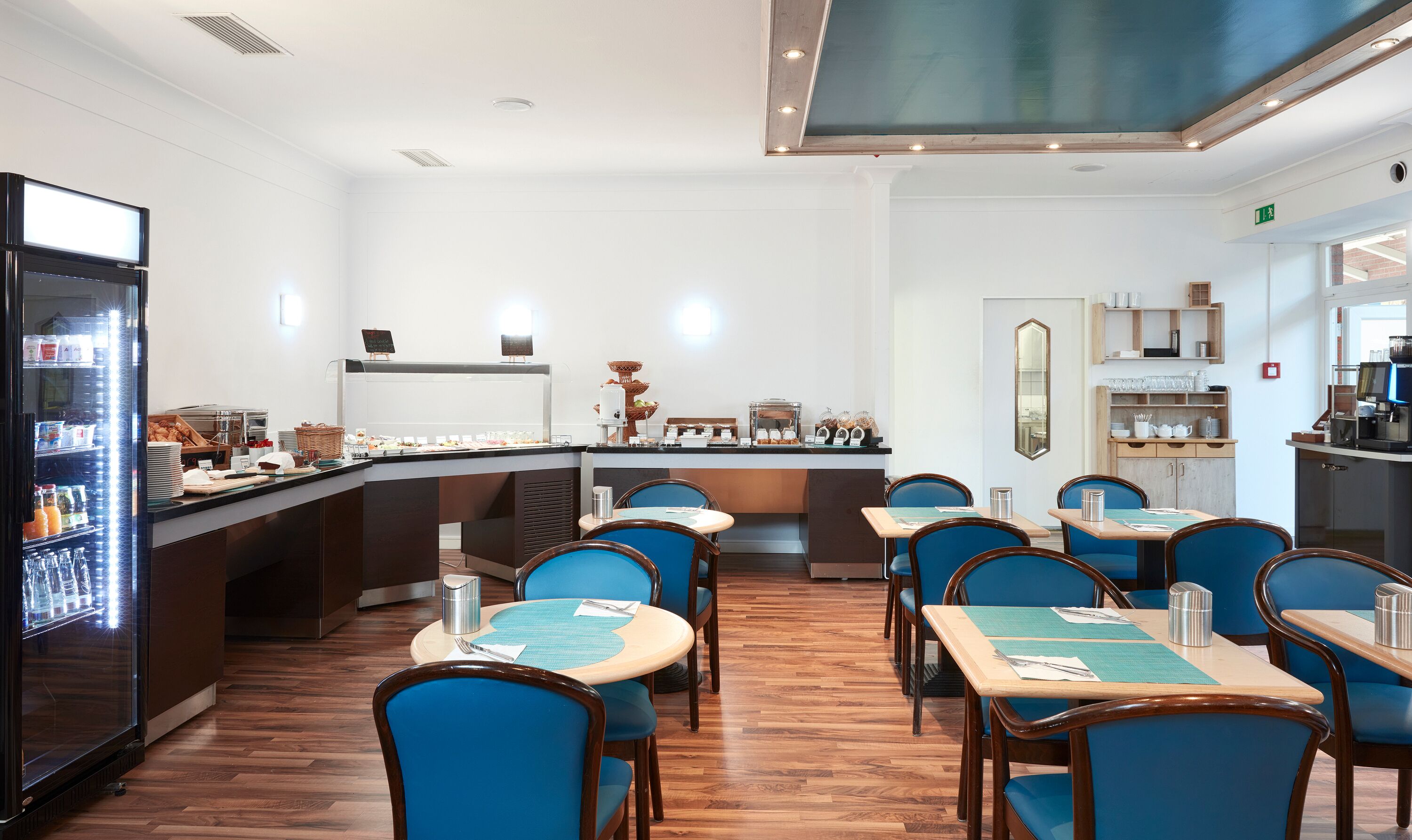 A restaurant with a buffet bar, blue chairs, and a coffee machine.